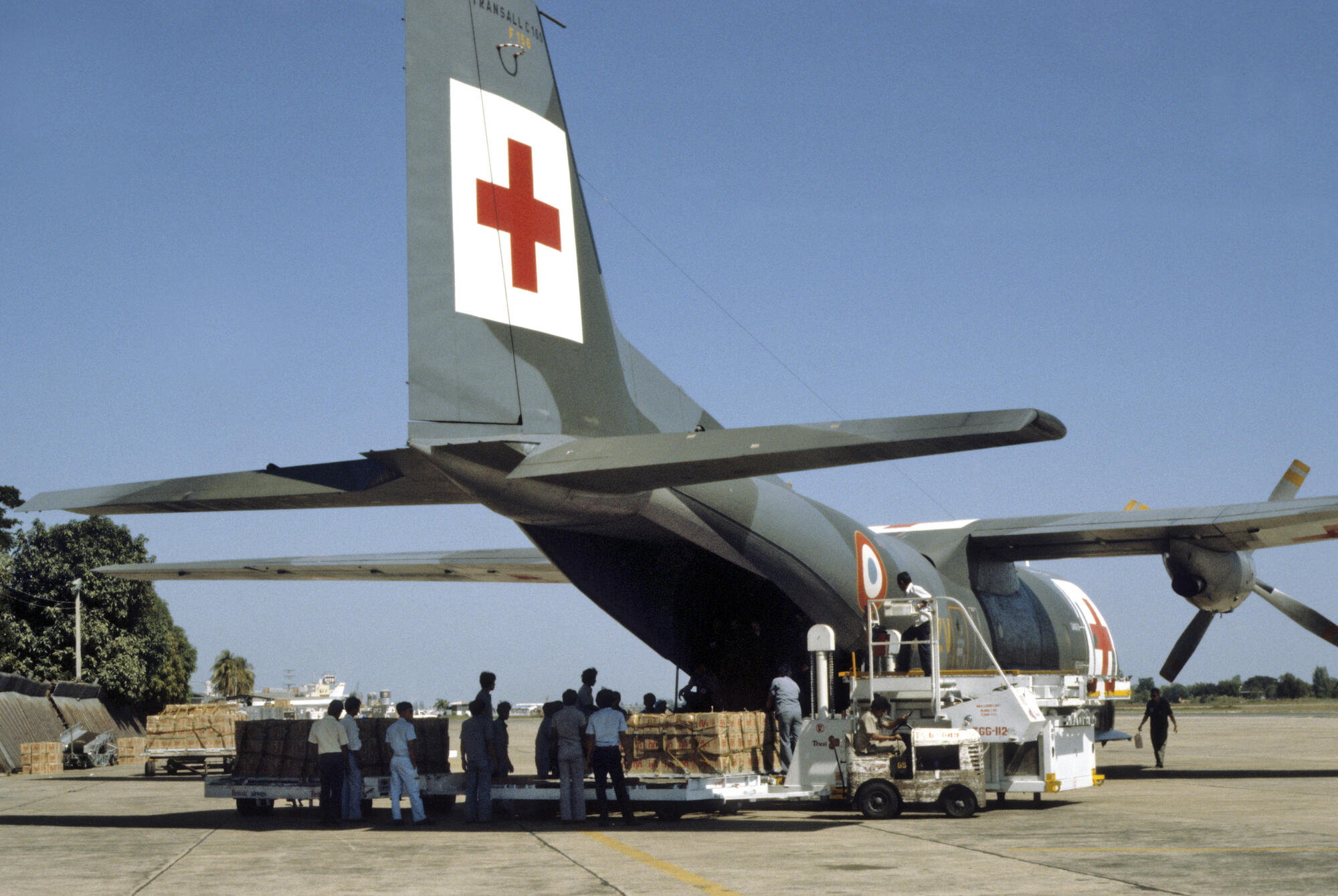 In the late 1970s war and civil strife had devastating effects on Kampuchea, causing hundreds of thousands of people to flee their homes and seek food and refuge in neighboring Thailand. UN relief agencies and cooperating independent groups responded to the crisis by helping to establish refugee camps along the border and taking in food, medical supplies and other essentials. More than 50 UN member nations, responding to appeals by Secretary-General Kurt Waldheim, donated over $200 million in 1980 alone to fund these efforts.
Medical supplies are unloaded from a Red Cross Plane at an airstrip in Thailand. The supplies will then be taken to refugee camps located along the border with Kampuchea. [No exact date]